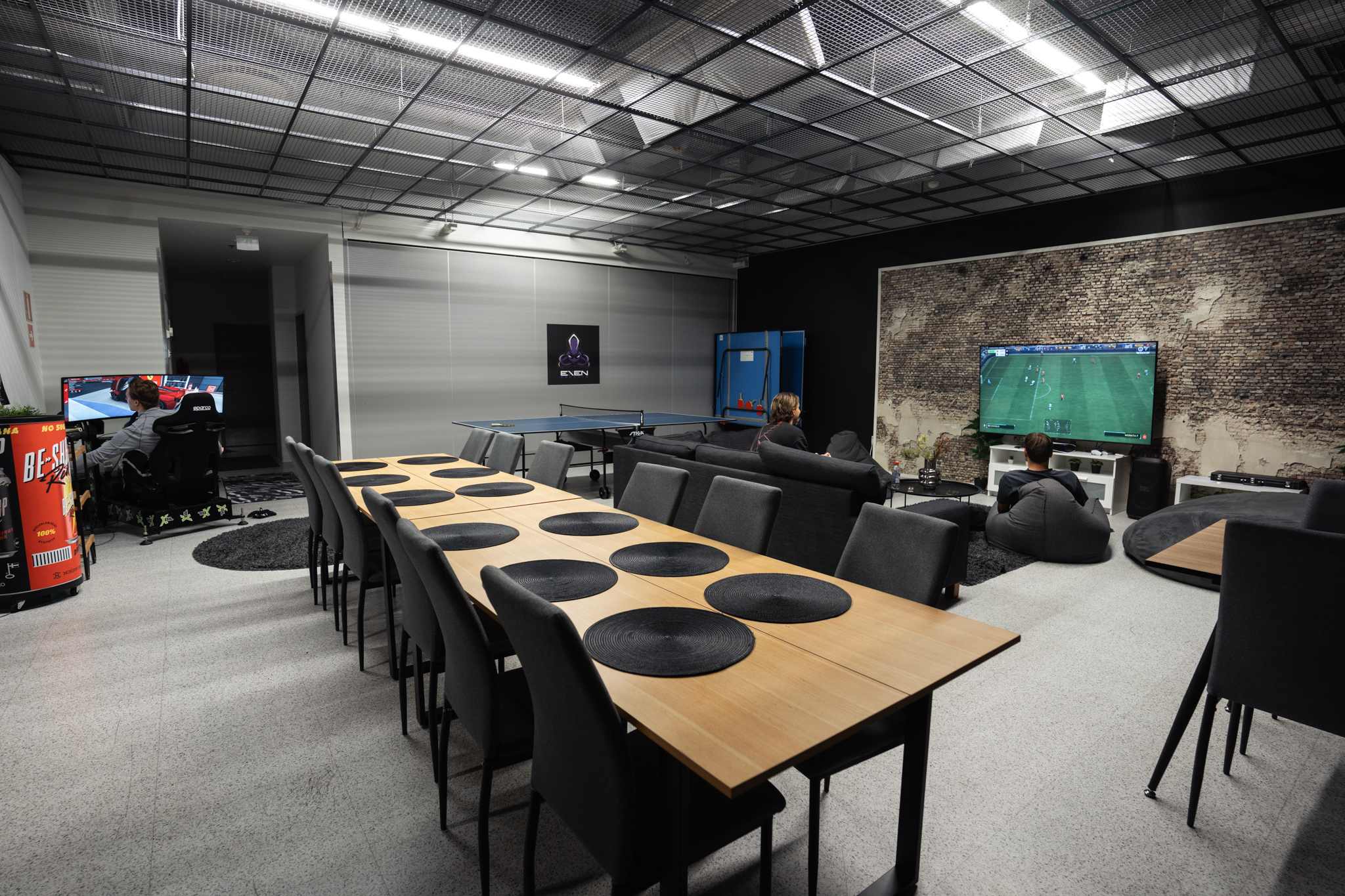 Lounge- ja keittiötila. Taustalla pelaajat pelaavat EAFC-peliä ja ajosimulaattoria